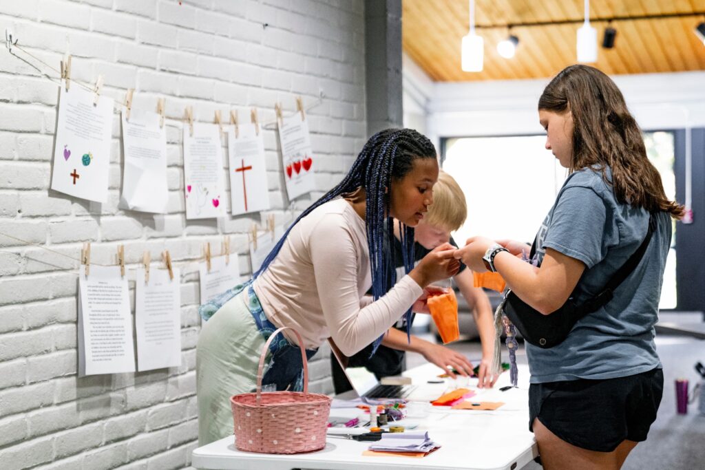 Bethel Community Education guide helping a middle school student with a craft project at a table at the Ada, MI campus