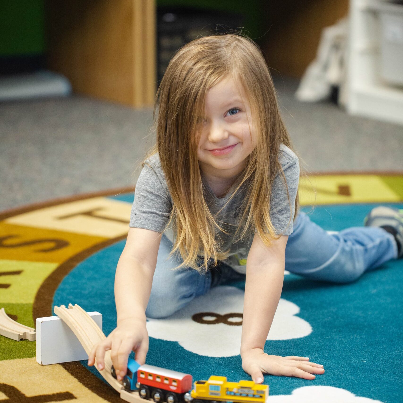 Bethel Community Education young girl playing with toy train on a classroom rug at the Rockford, MI campus